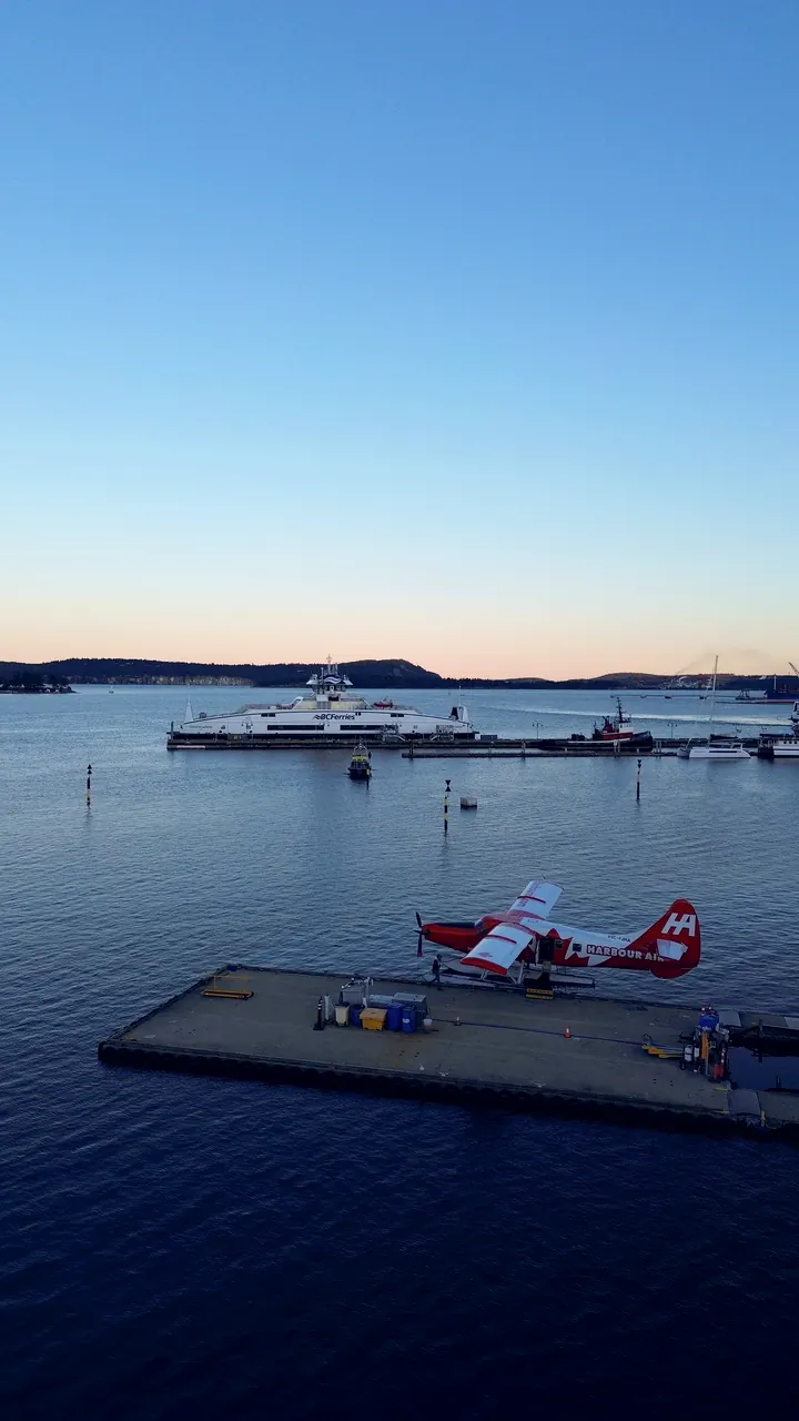 A floatplane on its dock with a ferry beyond, shot from above at dusk